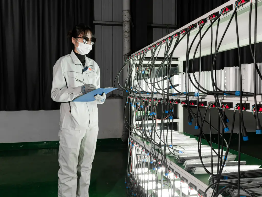 The module light source is laid flat on the aging instrument, and a worker wearing work clothes and holding a recording board is observing the light on