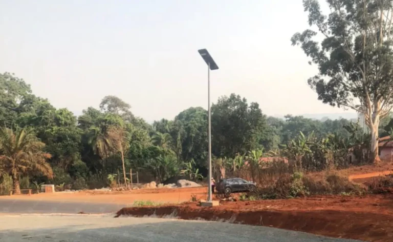 Solar street light installed beside a rural road curve with trees and red soil in Cameroon