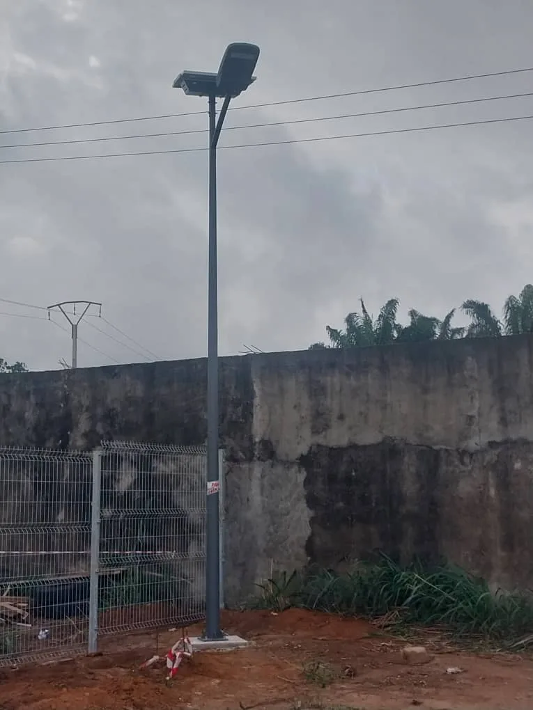 Daylight solar street light beside a fenced industrial site with overhead utility lines