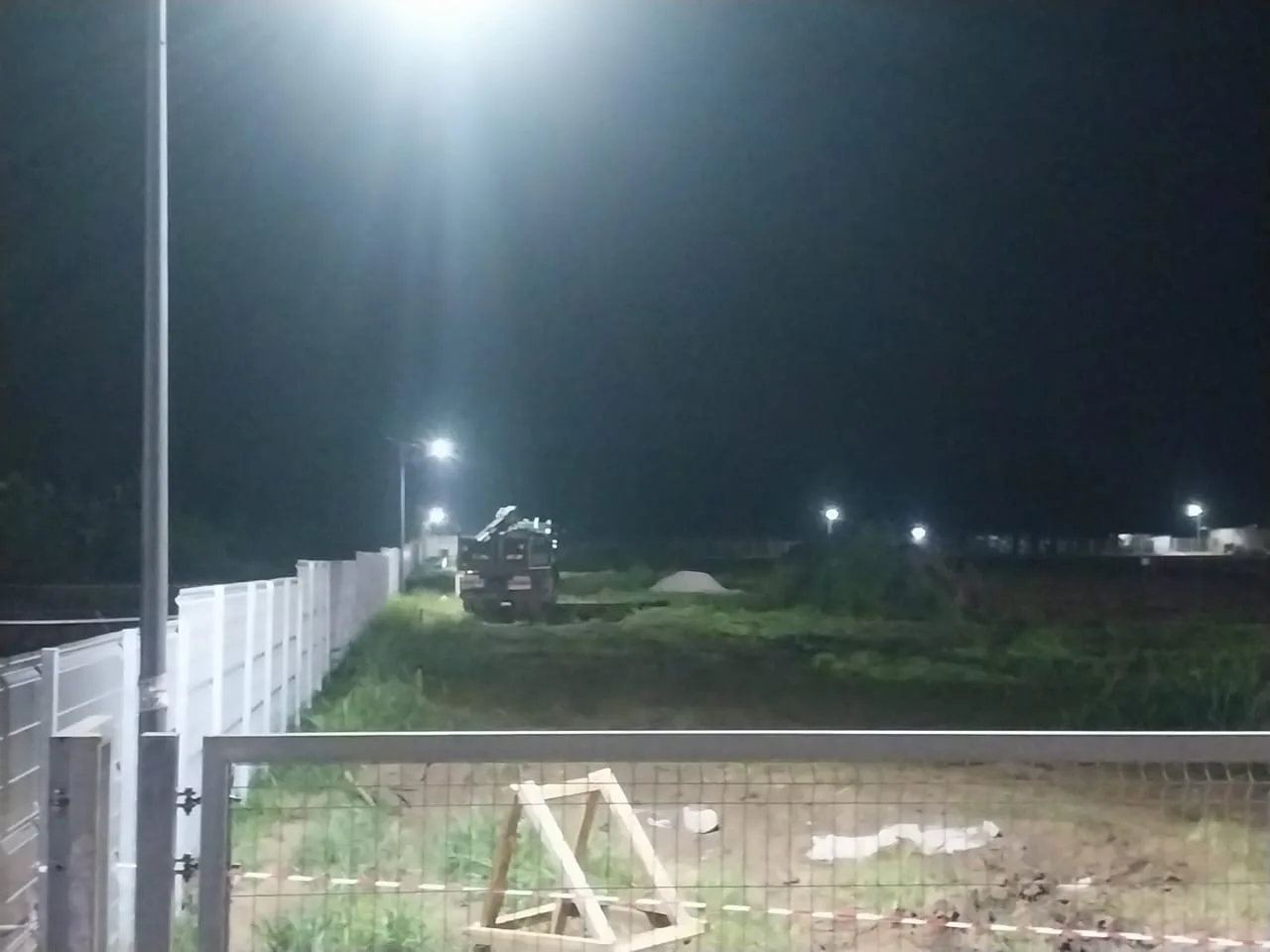 Night view of solar street lights illuminating a fenced industrial site and access area