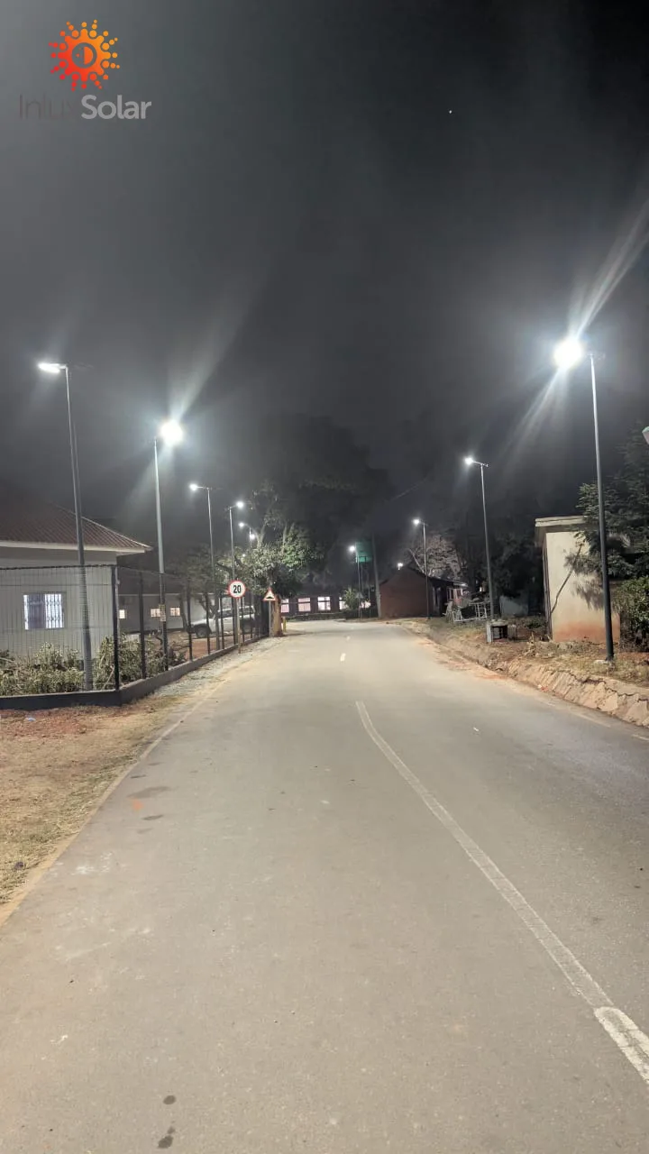 Solar street light illuminating an unpaved access road at night in a small Zambian town, with buildings and fencing nearby