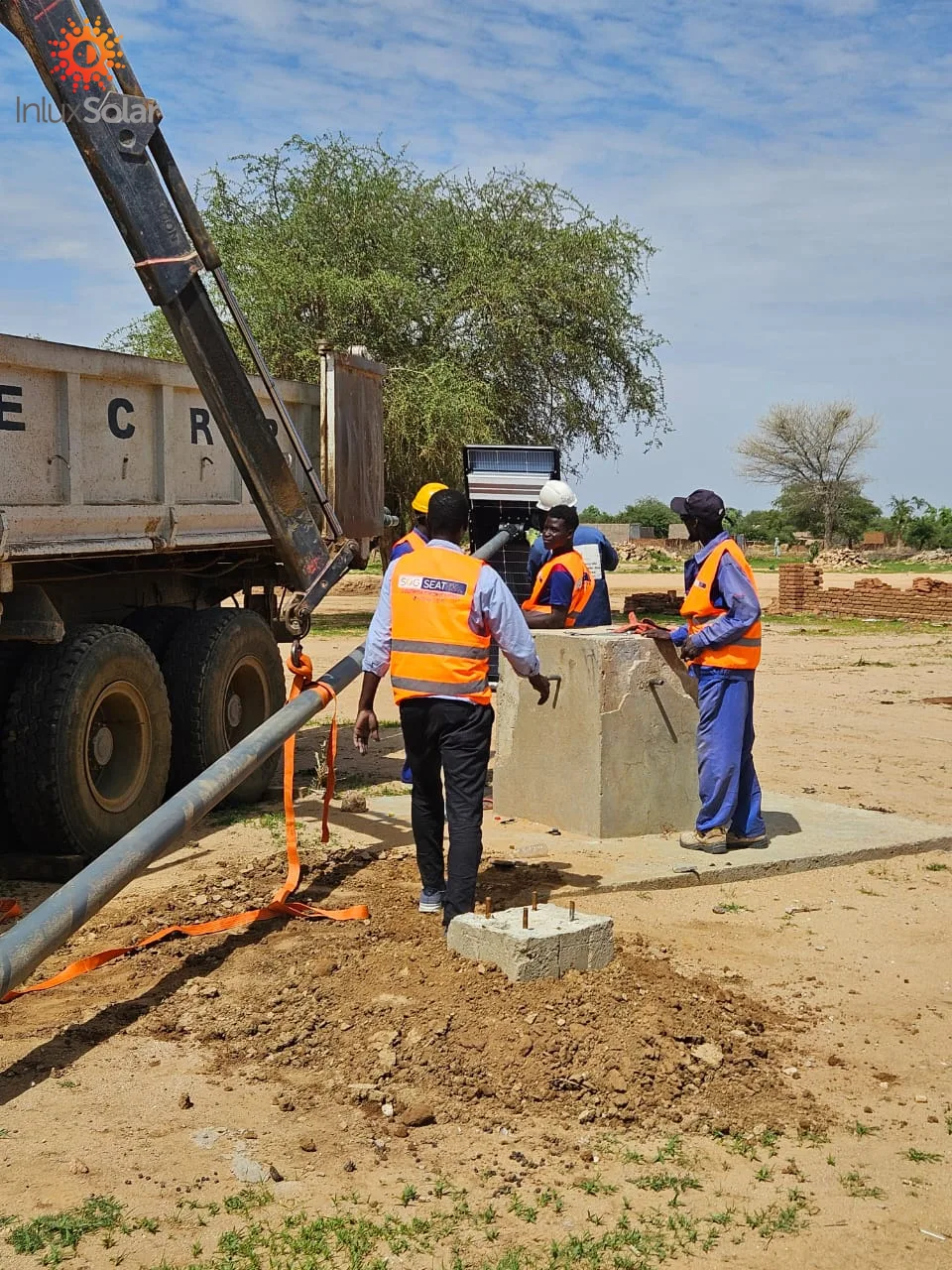 Installers positioning a solar street light pole beside its concrete foundation in Abéché